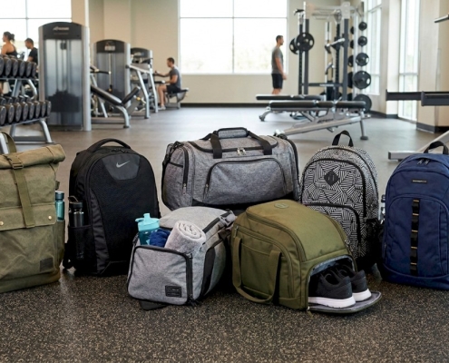 Array of gym backpacks in various styles, displayed on a gym floor with equipment in the background