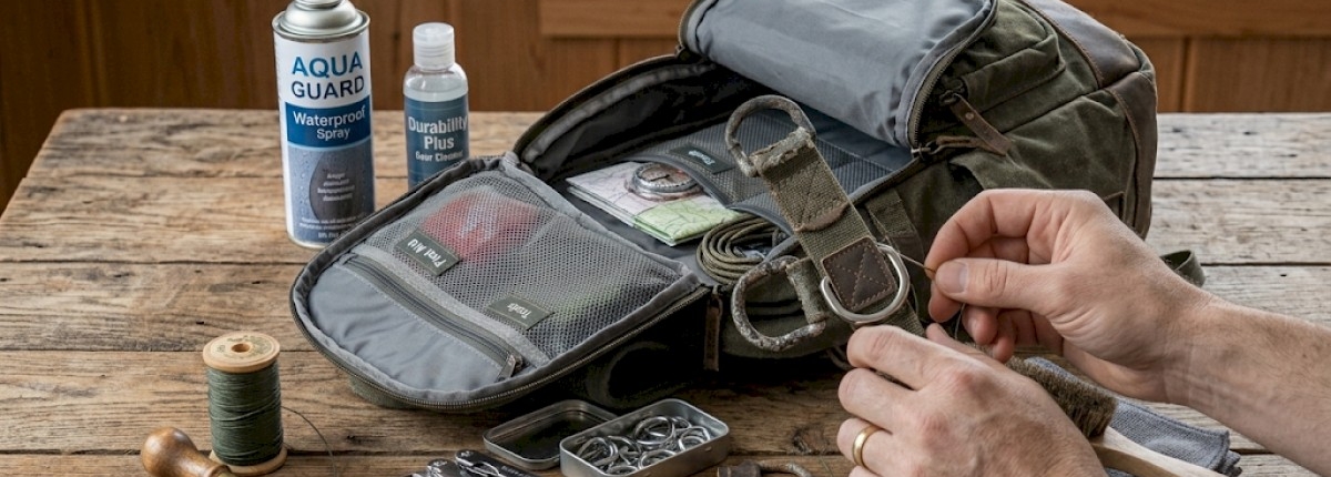backpack lying open on a wooden table with hand replacing worn D‑rings