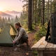 A beginner backpacker setting up a lightweight tent on a forest trail at sunrise