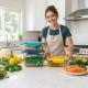 Colorful meal prep containers arranged on a kitchen counter with fresh vegetables and proteins