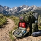 A compact hiking backpack open on a trail with neatly arranged gear and a mountain backdrop