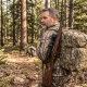 Hunter wearing a camouflaged backpack loaded with gear, standing in a forest clearing