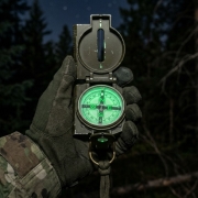 lensatic mil‑spec compass with a luminous dial in the hand at night