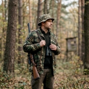 man wearing a military gear looking off into the distance while hunting in the forest during the day