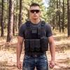 man-wearing-tactical-plate-carrier-vest-black-forest young man wearing a tactical plate carrier vest in black with a forest in the background during the daylight