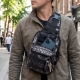 A sleek, black sling bag worn across the chest with a phone and keys visible in the front pocket
