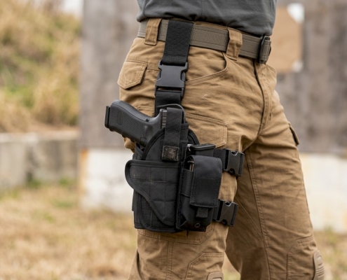 A tactical drop leg holster mounted on a thigh with a pistol visible, showing straps and modular pouches attached