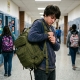 Teen adjusting MOLLE backpack straps in a school hallway