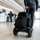 walking inside airport with carry-on molle backpack on wheels with airline checkout counter and people