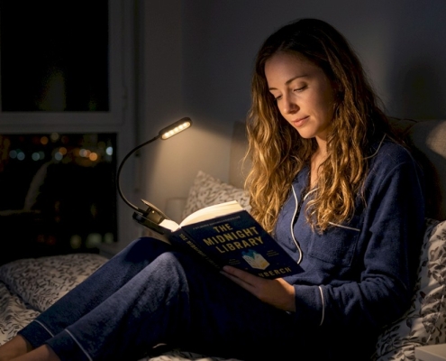 woman reading a book in bed at night with a clip-on rechargeable book light attached